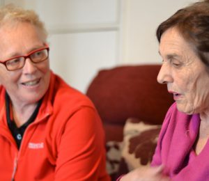 A volunteer advocate sits on a sofa chatting to a woman.